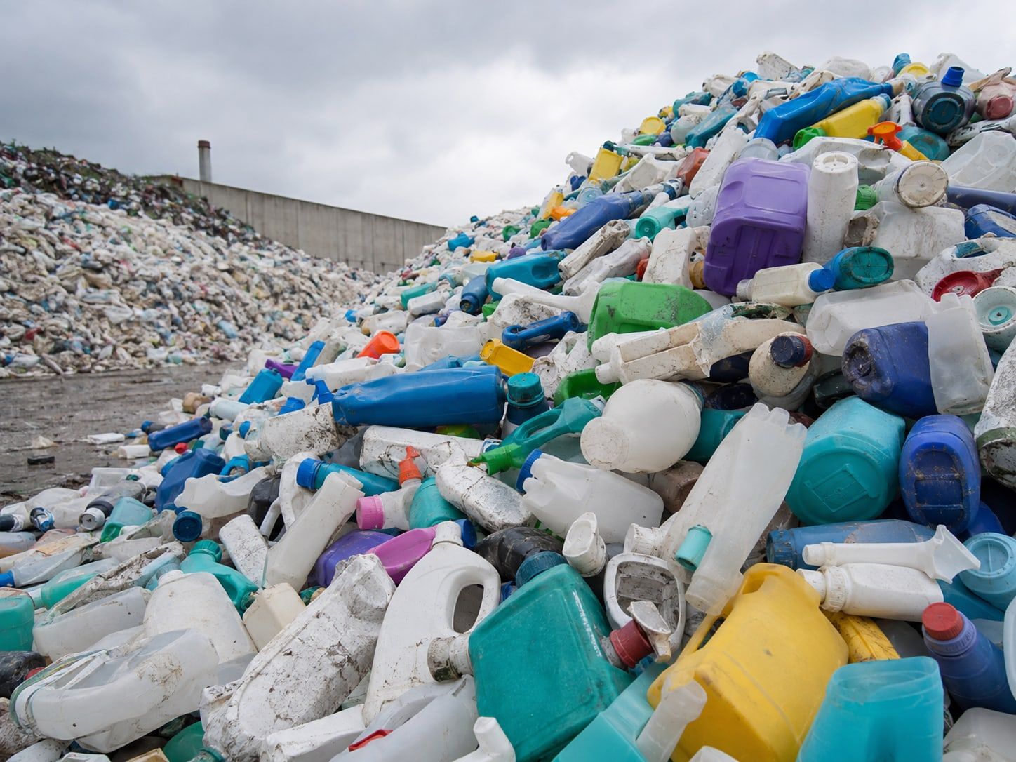 Berg aus leeren Kanistern und Flaschen von Reinigungsmitteln auf einer Deponie, im Hintergrund weiterer Plastikabfall