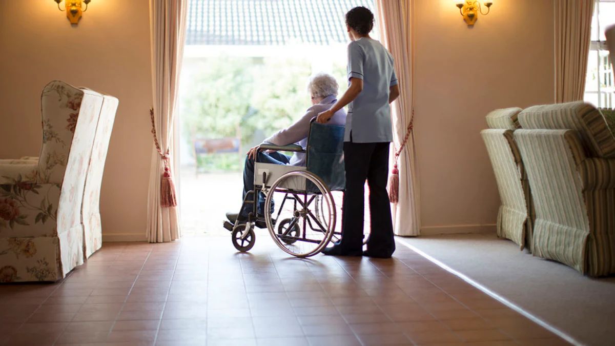 Pflegekraft begleitet eine ältere Person im Rollstuhl